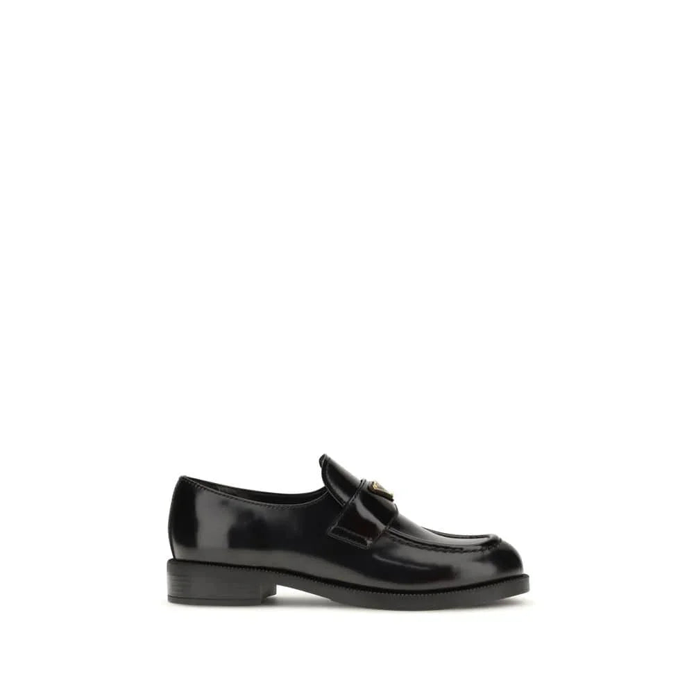 Black leather loafer with low heel and gold hardware on white background