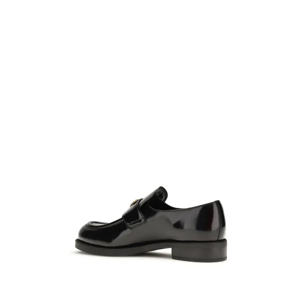 Black patent leather loafer with gold buckle detail on white background