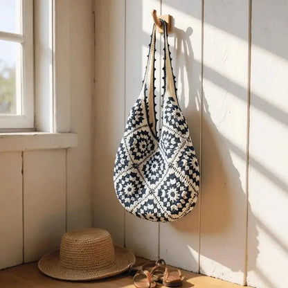 Hand-woven cotton yarn shoulder bag with geometric pattern hanging on a wall near a straw hat.