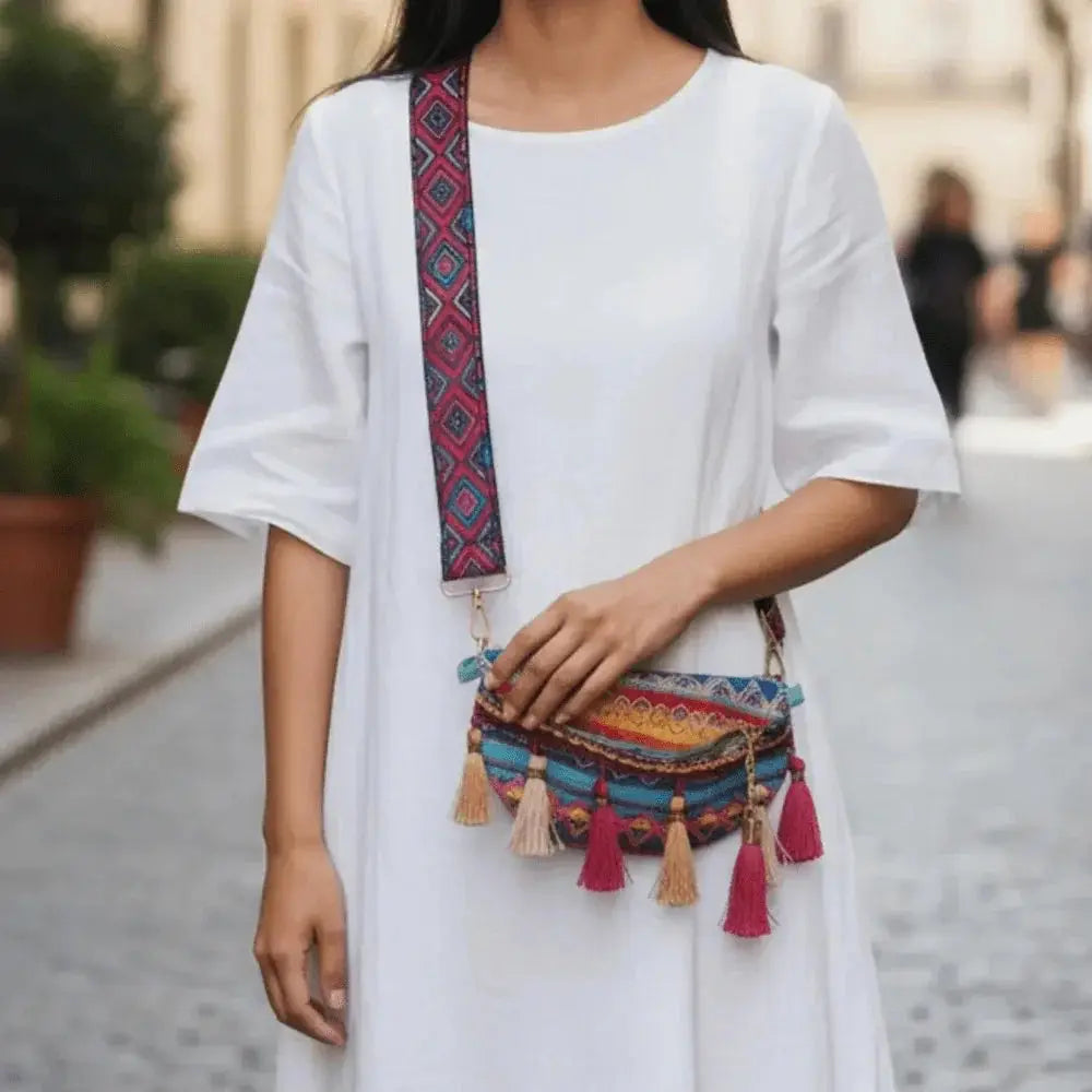 Colorful woven crossbody bag with decorative tassels and patterned strap, worn over a white dress