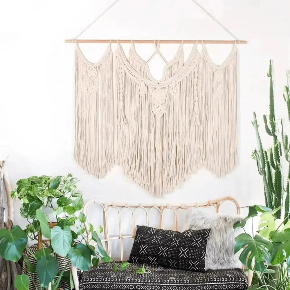 Large handmade macrame wall hanging boho tapestry above a boho-style sofa with plants