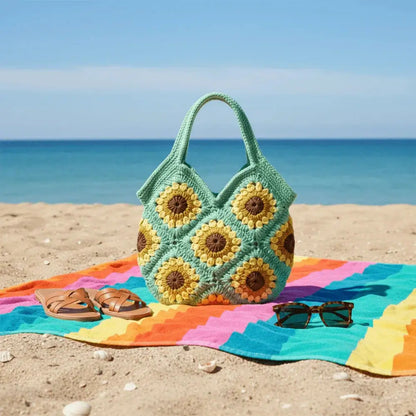 Handmade sunflower crochet bag on colorful beach towel, with sandals and sunglasses by the sea
