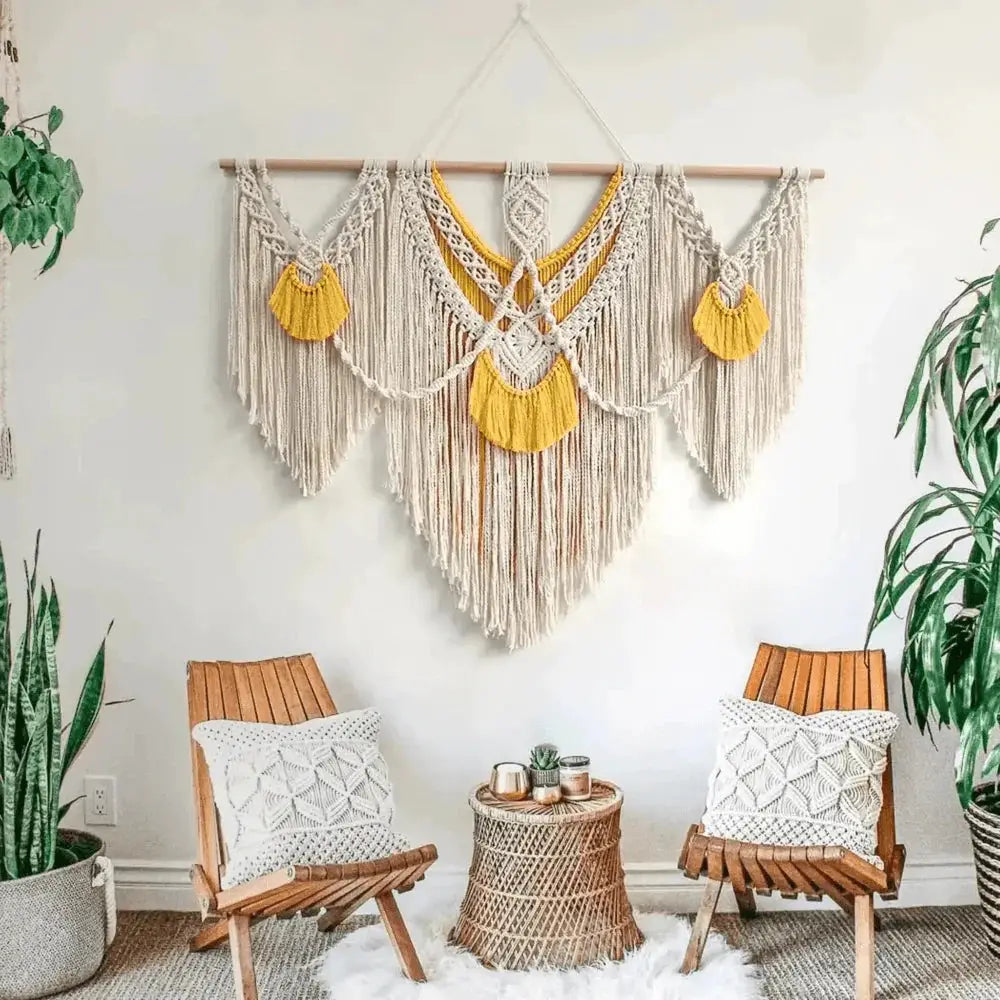 Large boho macrame wall hanging with yellow accents above wooden chairs in cozy living room