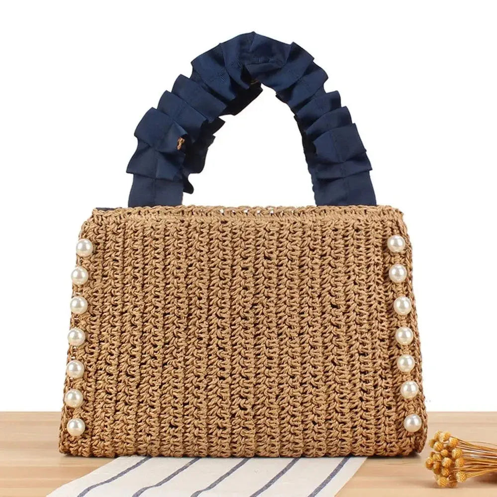Woven raffia tote bag with pearl accents and ruffle navy handles on a wooden surface
