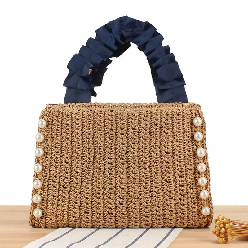 Woven raffia tote bag with pearl accents and ruffle navy handles on a wooden surface