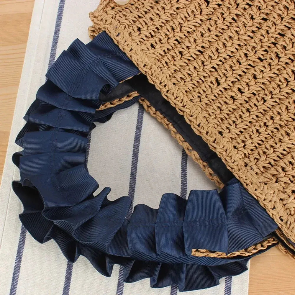 Woven raffia tote bag with navy blue ruffle handle on striped fabric background