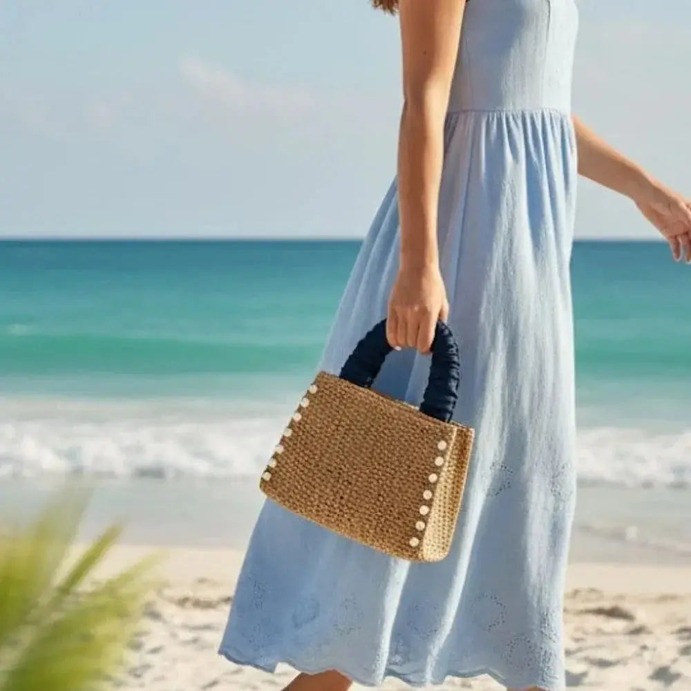 Woman holding woven raffia tote bag with ruffle handle and pearl accents on a beach