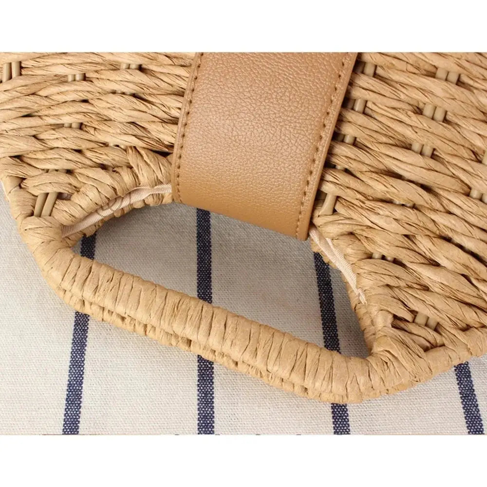 Closeup of woven straw crossbody bag with tan faux leather trim on striped fabric background