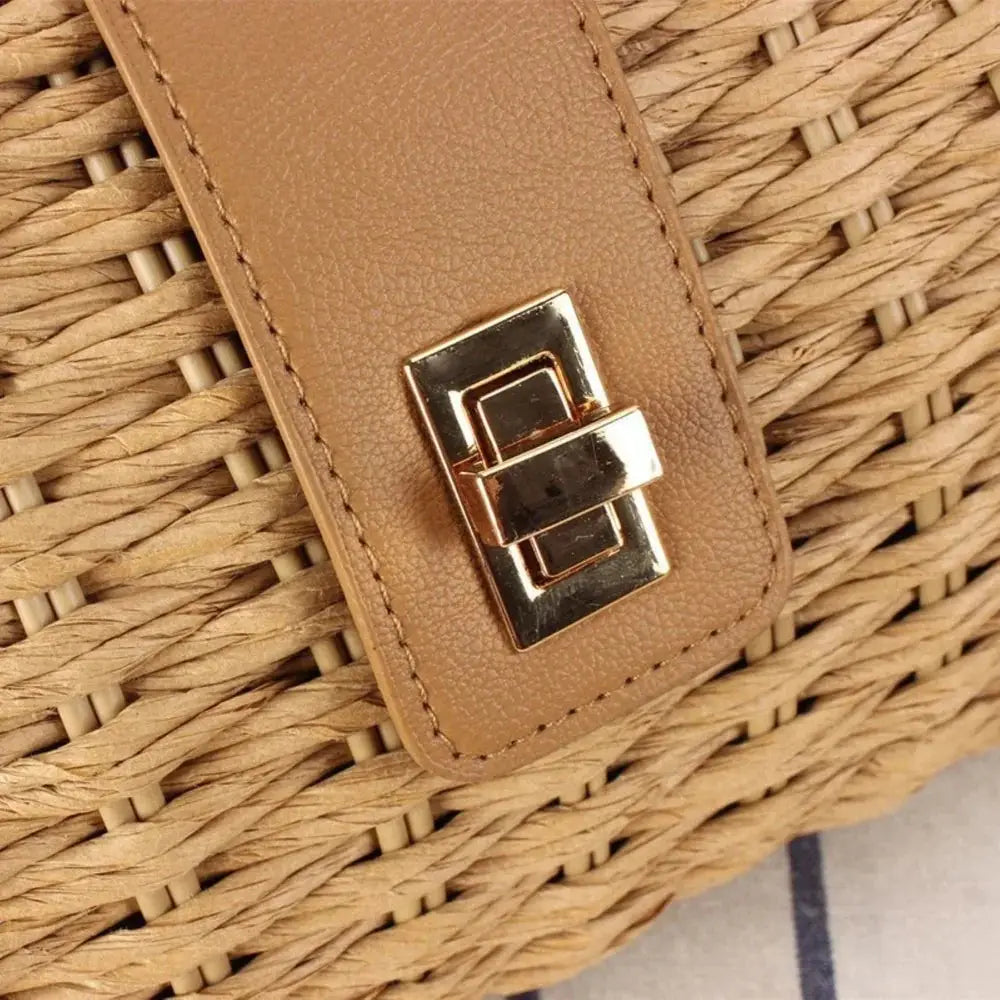 Close-up of woven straw crossbody bag with tan leather flap and gold turn-lock clasp
