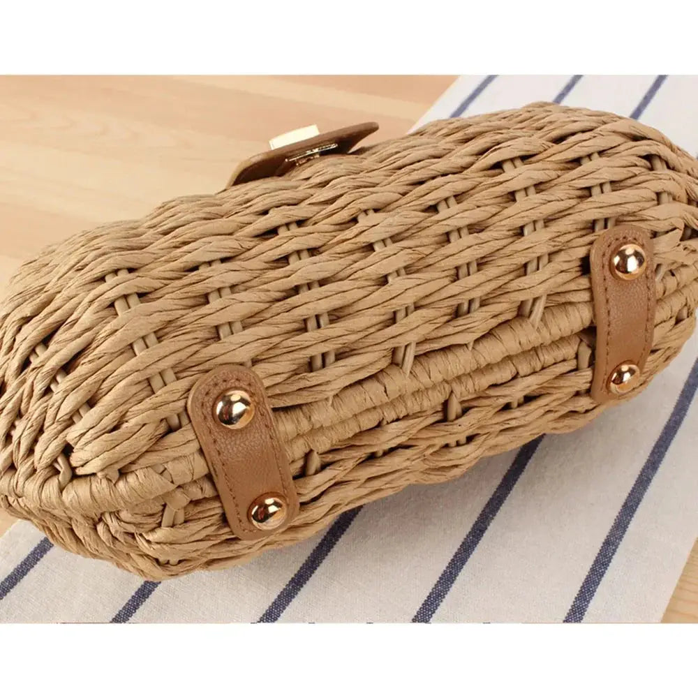 Woven straw crossbody bag with tan leather accents and gold studs on wooden surface