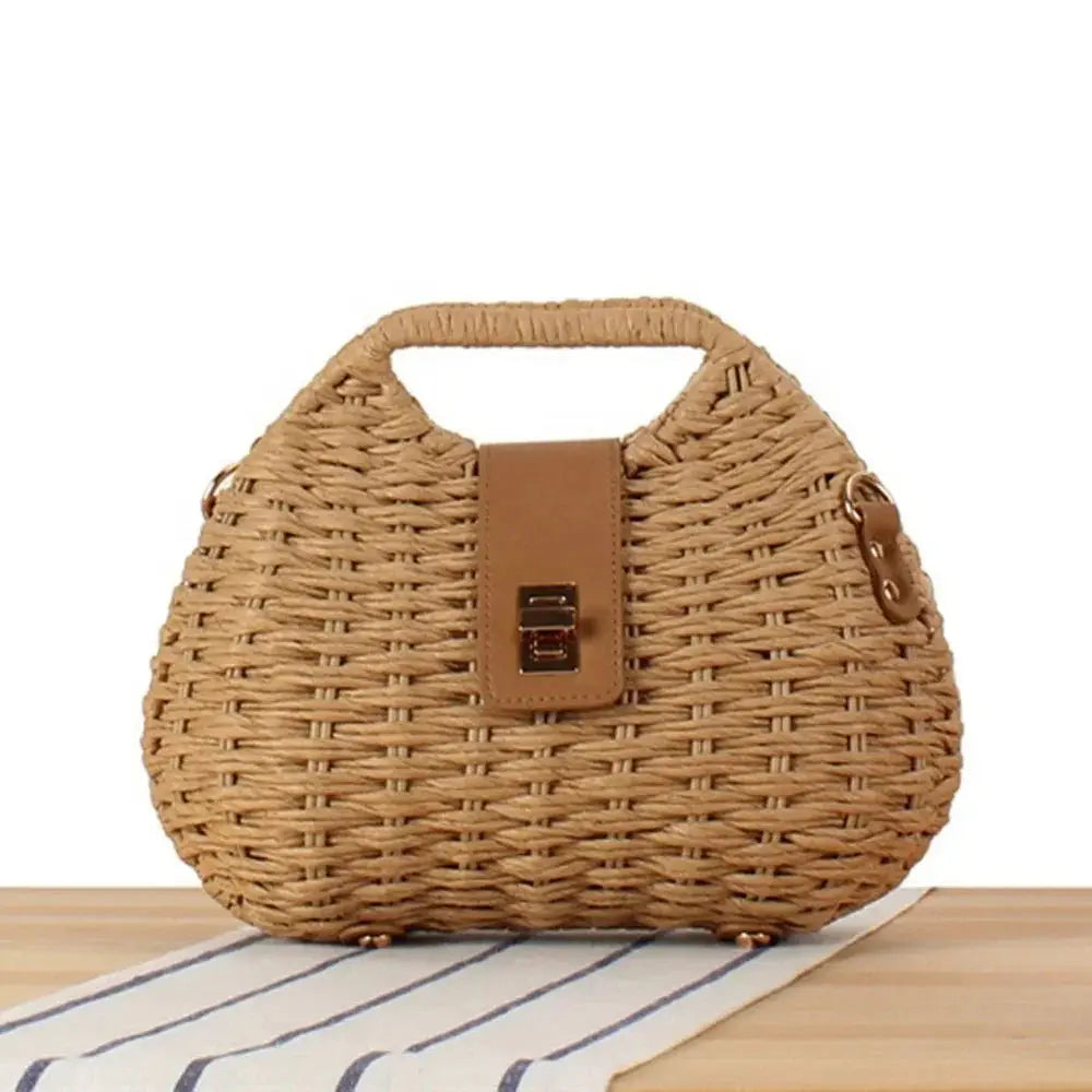 Woven straw box crossbody bag with top handle and brown buckle on table