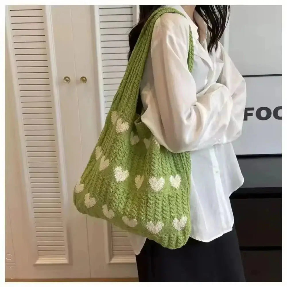 Green knitted tote bag with white heart patterns, worn on shoulder, soft cotton yarn