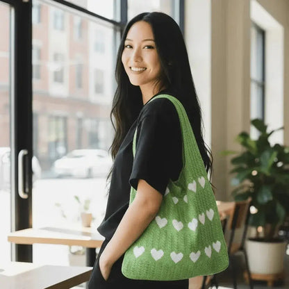 Woman carrying a green knitted heart tote bag made from soft cotton yarn indoors